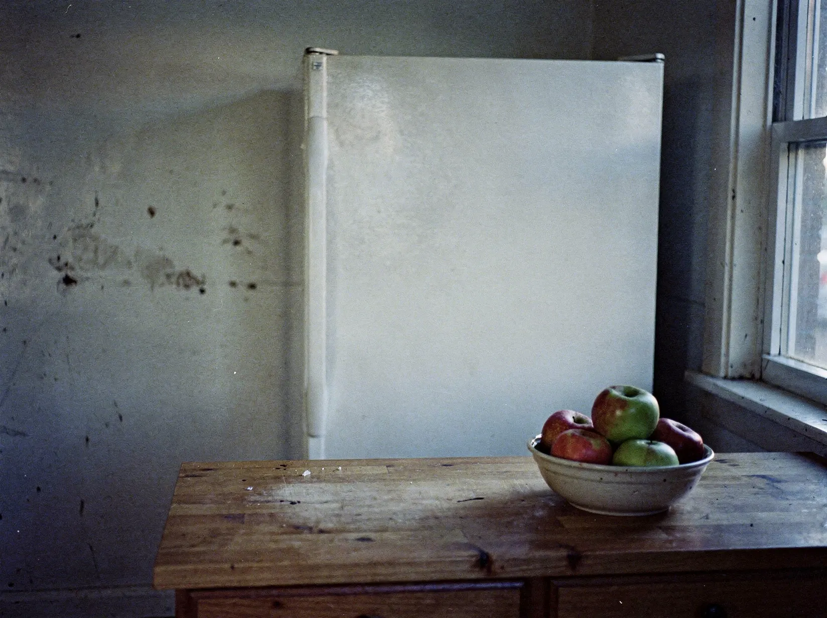 Küche in der Dämmerung mit geschlossenem weißem Kühlschrank an der Wand, daneben eine Arbeitsplatte mit einer Obstschale