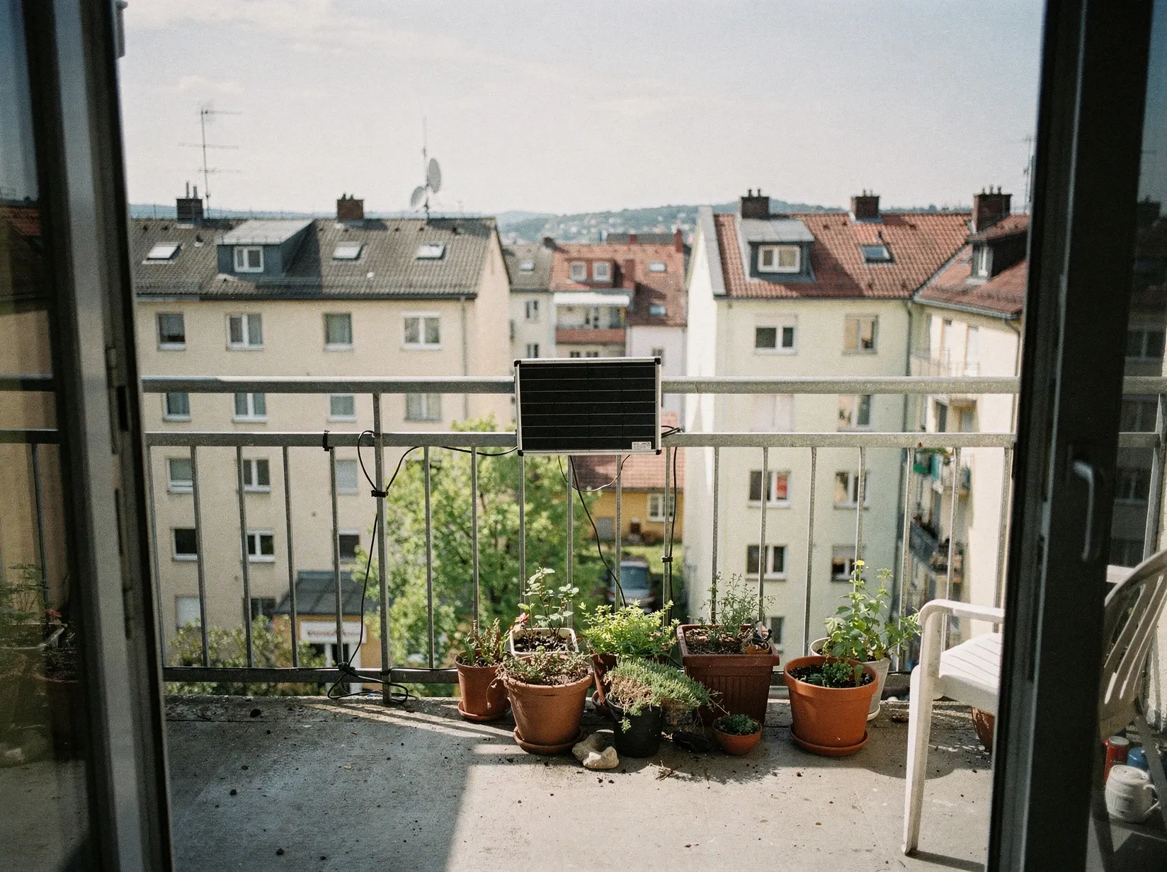 Blick von der Balkontür auf ein Solarmodul am Geländer, dahinter die Dächer einer Wohnstraße